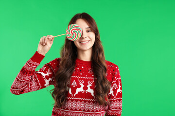 Smiling woman in sweater covering eye with lollipop on green background. Merry Christmas and Happy...