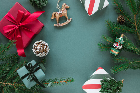 Overhead view of wrapped Christmas gift boxes, festive Christmas baubles, ornaments, pinecones and fir branches on a green background