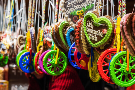 Hanging gingerbread hearts with messages and vibrant candy wheels on display at a European Christmas market stall. Selective focus
