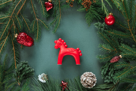 Overhead view of a red horse among festive Christmas baubles, ornaments, pinecones and fir branches on a green background