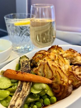 Close-up of an inflight meal consisting of shepherds pie and assorted vegetables with a glass of champagne and water