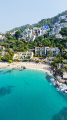 Tropical beach in mexico with clear turquoise water and coastal buildings on a lush hillside