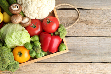 Different fresh raw vegetables and fruits in crate on wooden table, top view. Space for text