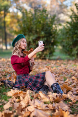 Pretty woman takes selfie using smartphone camera in autumn
