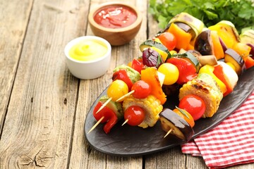 Skewers with tasty grilled vegetables and sauces on wooden table