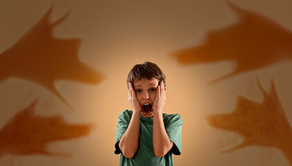 Scared little boy screaming during panic attack. Shadows of hands making dogs around him. Phobia, suffering from pathological fear