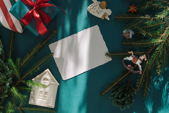 Overhead view of a blank deckle edge card with wrapped gift boxes, festive Christmas ornaments and fir branches on a green background