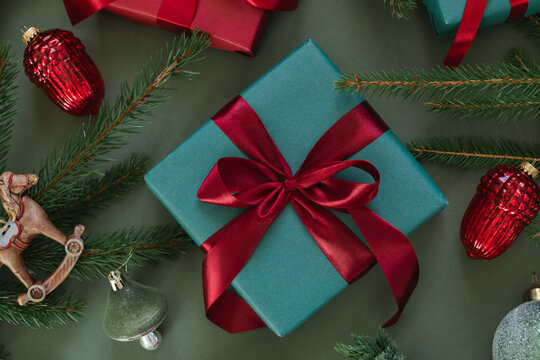 Overhead view of wrapped gift boxes with Christmas baubles, fir branches, pinecones and a Christmas tree ornament on a green background