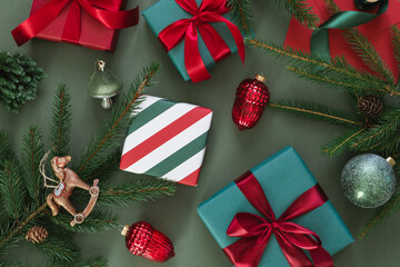 Overhead view of wrapped gift boxes with Christmas baubles, fir branches, pinecones and a Christmas tree ornament on a green background