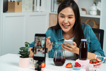 Smiling young beautiful Asian reviewing tasty mixed strawberry and cherry juice detox drinks,...