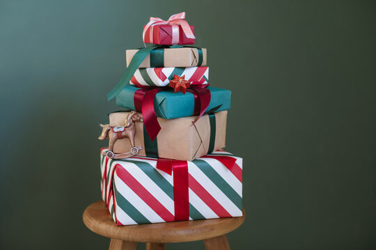 Close-up of a stack of five wrapped Christmas gifts with fairy lights on a wooden stool