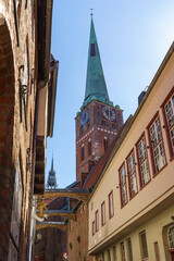 A tall building in Lubeck Germany with a clock tower and a green spire. The building is old and has a lot of windows