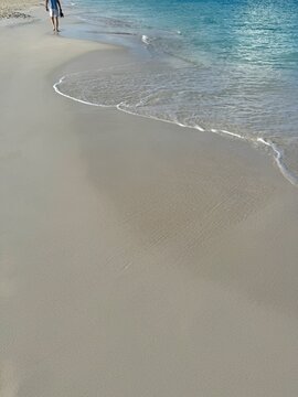 Distant rear view of a barefoot man walking along a tropical sandy beach, Eagle Beach, Aruba
