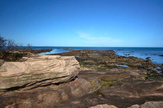 Seacliff Beach in East Lothian under clear blue skies, rugged rocks and tranquil sea.