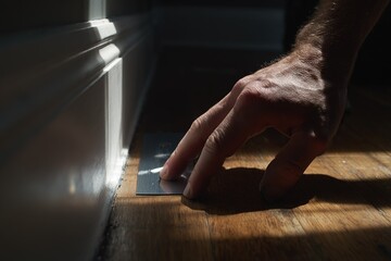 Hand applying finishing touches to baseboard in a dimly lit room during early evening hours