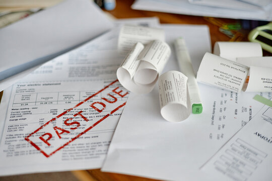 Closeup showing multiple utility bills and invoices scattered on desk, including electric statement marked past due, emphasizing financial analysis and overdue payment context