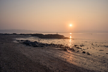 A tranquil sunset casts warm light over the rocky shore at Cramond Island, Edinburgh.