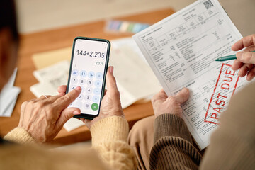 Naklejka premium Two adult men analyzing overdue invoice, one holding smartphone with calculator app, other holding bill marked past due, focusing on financial calculations together