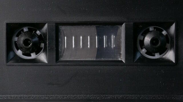 Black cassette tape playing a tape deck, the last popular form of analog tape media. Close op of small reels turning.