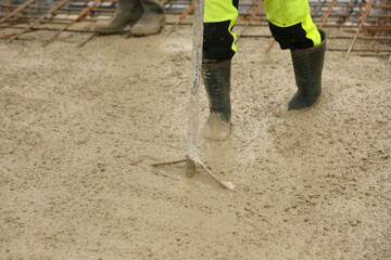 Construction worker leveling freshly poured concrete in a building foundation