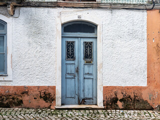 Vintage blue double doors with ornate ironwork on textured white wall, traditional Portuguese architecture and rustic street scene in southern Europe