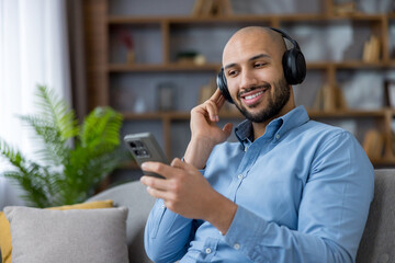 Smiling man listening to music on headphones using phone at home