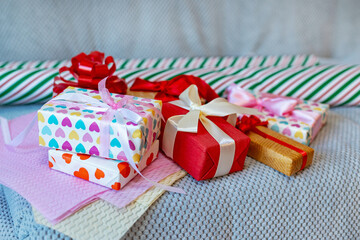 Colorful wrapped gift boxes with ribbons on bed. A variety of brightly wrapped gift boxes with bows and ribbons are arranged on a bed with wrapping paper rolls in the background.