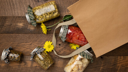 Yellow daisy flowers and Food items preserved in glass jars spilling out of a brown, reusable shopping bag. Farmer's market concept.