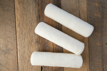 Three white woven fabric paint rollers on a wooden background.