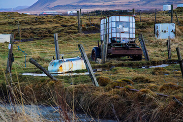 Old farm equipment and water tanks on rural field in Akranes, Iceland