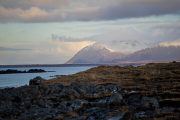 Snow-capped mountains and rocky coastal landscape at sunset, Akranes, Iceland