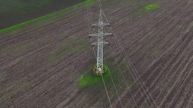 Aerial drone view of power transmission lines stretching across open terrain, tall pylons and cables forming strong linear patterns that highlight energy distribution and industrial landscape.