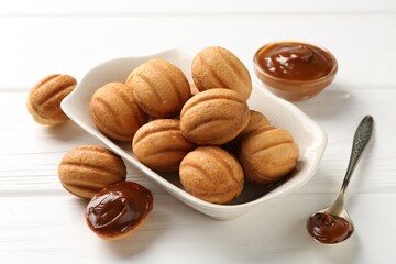 Delicious nut shaped cookies with boiled condensed milk and spoon on white wooden table, closeup