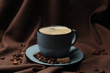 Aromatic coffee in cup, beans and brown sugar on fabric, closeup
