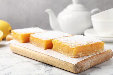 Tasty lemon bars with powdered sugar served on white marble table, closeup