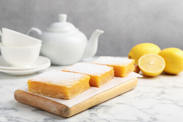 Tasty lemon bars with powdered sugar served on white marble table, closeup