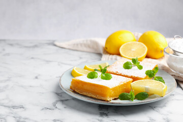 Tasty lemon bars with powdered sugar, mint and fresh fruits on white marble table, closeup. Space for text