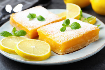 Tasty lemon bars with powdered sugar, mint and fresh fruits on grey table, closeup