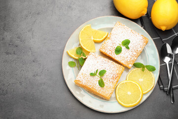 Tasty lemon bars with powdered sugar, mint and fresh fruits on grey table, flat lay. Space for text