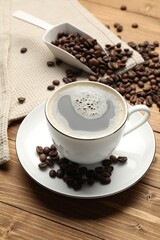 Aromatic coffee in cup and beans on wooden table, closeup