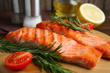 Pieces of tasty grilled salmon, rosemary and tomatoes on table, closeup