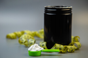 Black jar filled with white powder and green scoop, placed on a surface with yellow measuring tape, representing fitness, health, and nutrition themes for active lifestyles