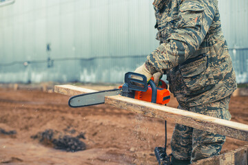 A man saws a board for formwork with an electric chain saw. Photos on the topic Construction and laying the foundation. High quality photo