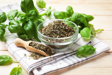 Dry basil leaves, fresh ones, bowl, scoop and napkin on light wooden table, closeup