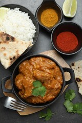 Delicious chicken tikka masala, rice, cilantro, lime, lavash and spices on grey textured table, flat lay