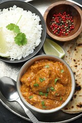 Delicious chicken tikka masala, lavash, cilantro, rice, lime and peppercorns on grey table, top view
