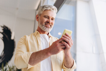 Happy, smiling gray haired man, businessman holding mobile phone using mobile app, text message