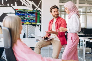 Smiling managers, bearded man and muslim woman wearing hijab holding clipboard talking together