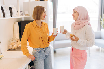 Beautiful women wearing casual clothes talking, having coffee break, standing in modern office