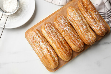 Tasty eclairs with powdered sugar on white marble table, top view